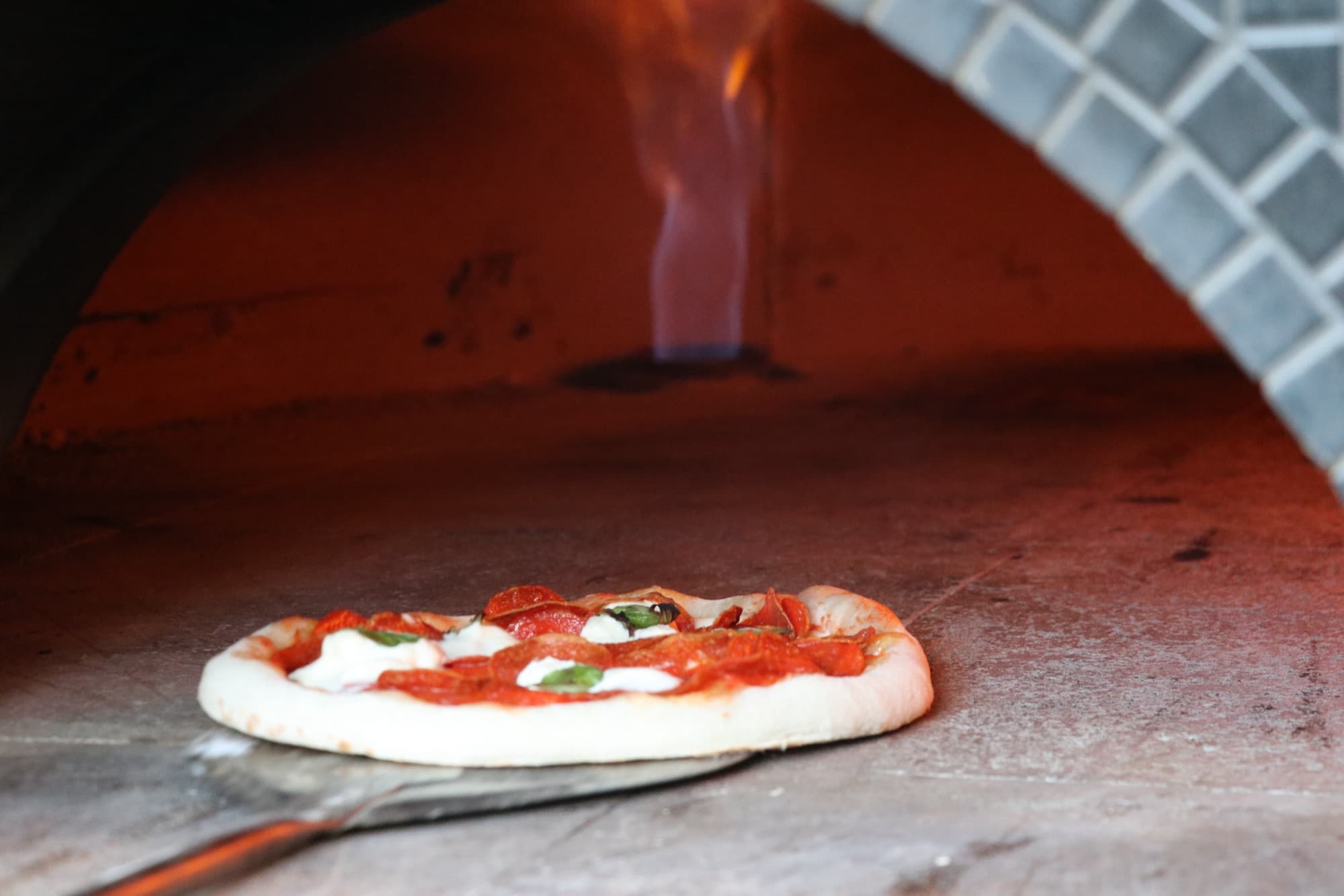 A margherita pizza baking in the wood-fired oven with live flame at Rising Phoenix Taproom