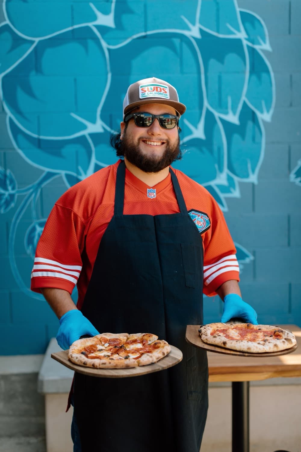 A Rising Phoenix pizzaiolo holding two wood-fired pizzas